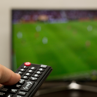 a remote pointed at a TV screen showing a sports game
